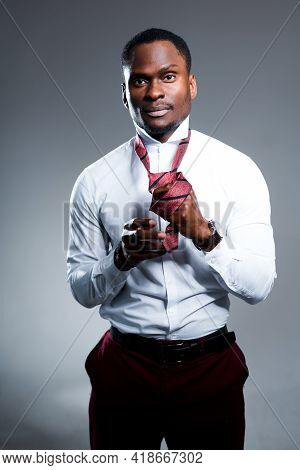 Attractive African American Man In A White Shirt Holds A Tie In His Hands And Ties It Around His Nec
