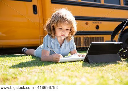 Portrait Of Little Schoolboy Writing Outdoor In Schoolyard Park And Doing Homework.