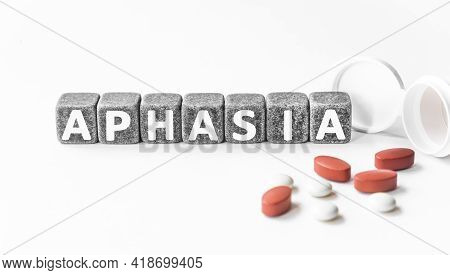 Word Aphasia Is Made Of Stone Cubes On A White Background With Pills. Medical Concept Of Treatment, 