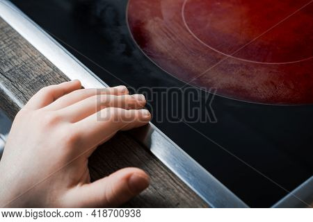 Hand Of A Child Reaches Active Hotplate Of A Kitchen Glass-ceramic Stove - Prevent Child Hazard Conc