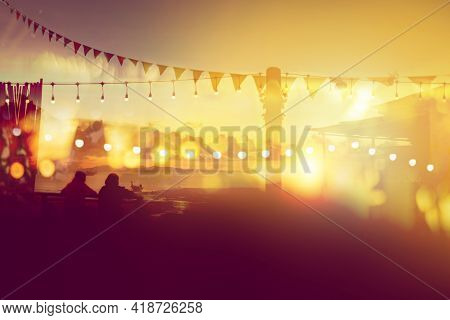 Two Friends Watching Sunset At Restaurant On The Beach, Blurred Bokeh Light On Sunset With Yellow St
