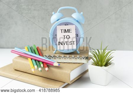 Time To Invest - Business Concept Holding Clock On Blurred Bookstore As Background