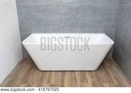A Modern, Free-standing Wall-mounted Bathtub, Without A Tap, Standing In A Bathroom Lined With Ceram