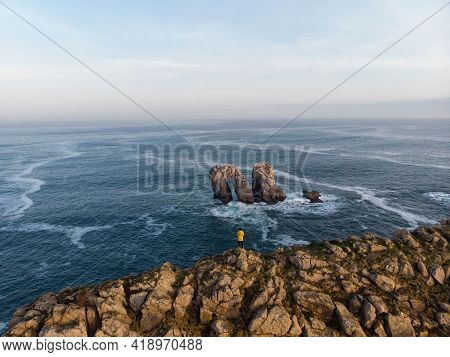 Young Male Tourist In Yellow Jacket At Urro Del Manzano Rock Formation Sea Stack Natural Arch Bridge