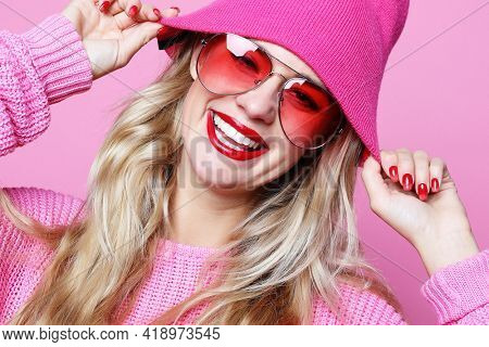 fashion portrait of trendy casual young woman in pink pulover and hat, posing over pink background. Hipster style.