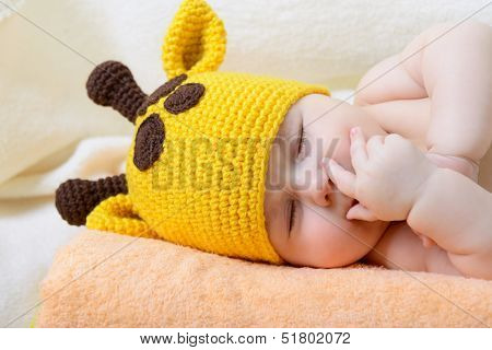 cute sleeping baby boy in funny hand made giraffe hat, beautiful kid dozing on plaid, studio shot
