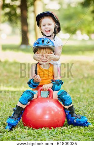 Little boy sits on red ball for jumping, girl closes his eyes with her hands, standing behind him