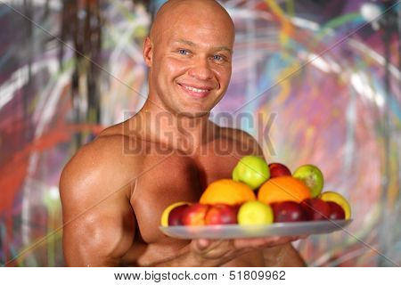 Muscular bald man with a naked torso with a plate of fruit in hand