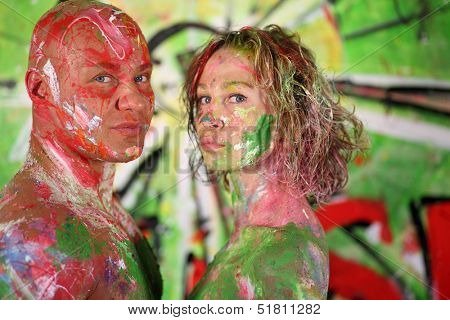 Naked girl and bald man all in the paint in studio