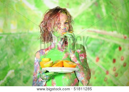 Young girl covered in paint eating an orange in studio