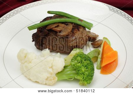 Beef tournedos (tenderloin fillet steak) served with mushrooms, steamed beans, courgettes, cauliflower, carrot and broccoli, a minimalist modern take on a traditional favourite.