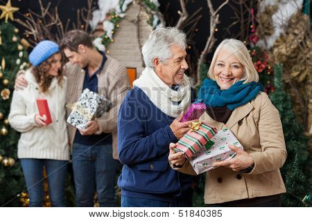 Portrait of happy senior couple holding Christmas presents with children standing in background at store