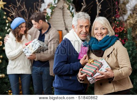 Portrait of senior couple holding Christmas presents with children standing in background at store