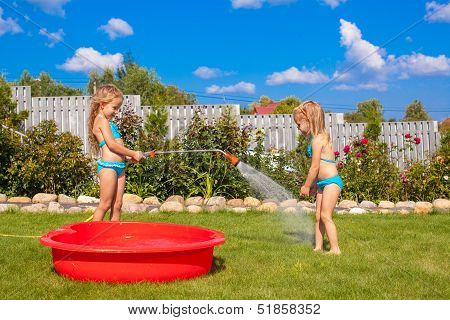 Two Little Sisters Frolicing, Splashing And Having Fun In Their Yard