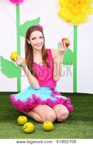 Beautiful young woman in petty skirt with apples on decorative background