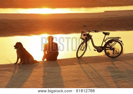 Silhouetted Man With A Dog Watching Sunset At Mekong River Waterfront, Vientiane, Laos