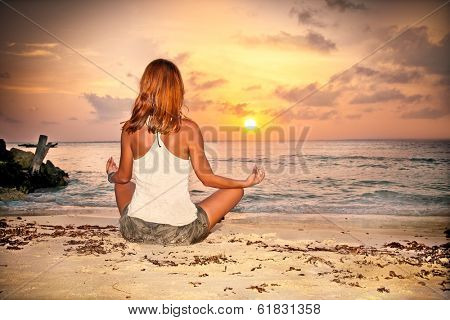 A relaxed sexy young brunette woman sitting on a deserted tropical beach at sunset 
