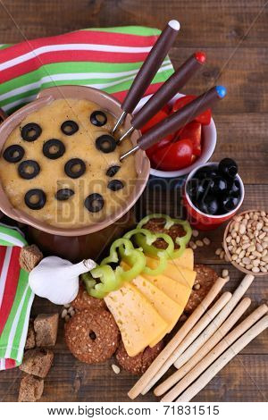 Fondue, olives, tomatoes, slices of cheese, rusks and spices on napkin on wooden background