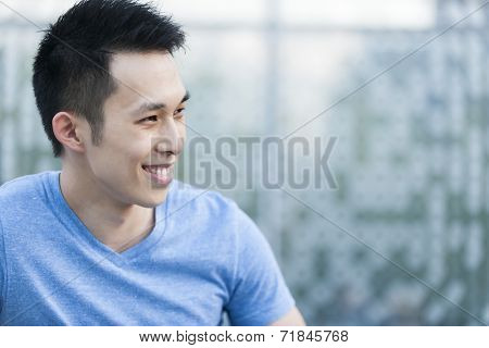 Portrait of confident young asian man in profile smiling on blue background with copy space