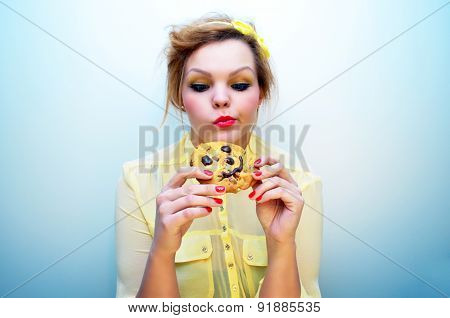Trendy young woman is eating a smiling chocolate chip cookie.