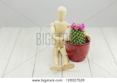 Blooming cactus in a flower pot and a mannequin on a wooden table.