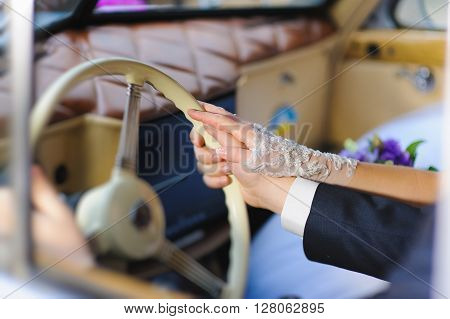 Women's and men's hand on steering wheel of a retro car. Bride in transparent gloves. Groom in a suit, white shirt and cuffs. A couple in a retro car.