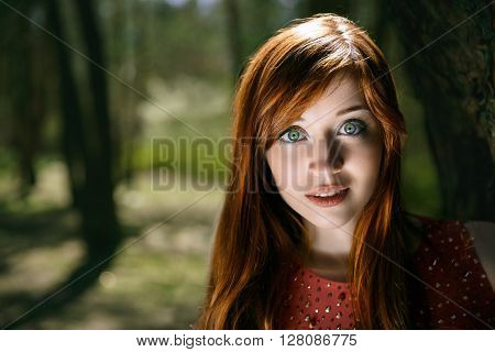 The smiling girl with big green eyes looks out a tree.