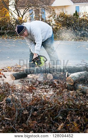 Man cutting tree limbs with a chainsaw that have fallen from storm damage.  A late fall snow storm in the month of October was the cause.