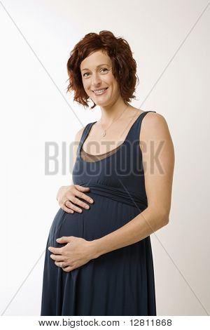 Porträt von Lüneburg Mid schwangere Frau mit Hände auf Bauch Viewer betrachten und lächelnd.