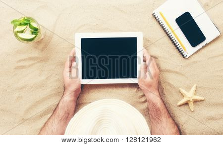Man holding tablet with blank screen lying on the beach. Man communicates via the Internet using the tablet relaxing on the beach. Top view