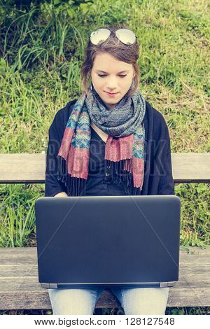 Young woman using laptop at a riverbank. Milleanial working in a park.