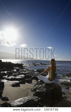 Jóvenes adultos asiáticos Filipino mujer meditando en una playa rocosa en Maui Hawaii.
