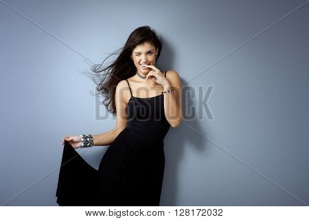 Sexy girl posing by grey wall, winking, biting finger impish.