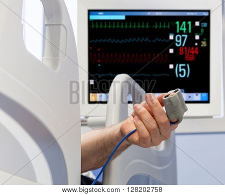 Patient's Hand in Bed with Oximeter and Monitor on Background
