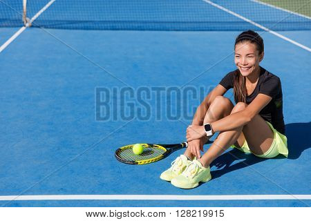 Tennis player woman wearing sports smartwatch. Beautiful sport athlete portrait resting on blue outdoort hardcourt relaxing happy with wearable tech wristwatch for activity tracker on fitness workout.