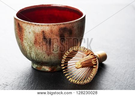 Ceramics bowl and chasen - special bamboo matcha tea whisk, lying on black stone background