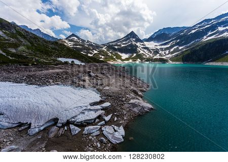 Weissee in Alps beautiful lake in Austrian mountains. Turquoise lake high in mountains. Frozen snow in foreground