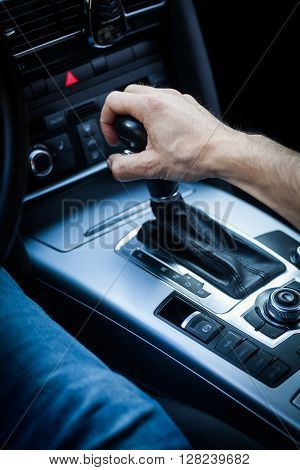 Detail of a hand pulling an automatic gear shifter in a new car.