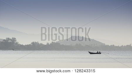 Silhouetted Fishing Boat Showing Misty Mountains Early Morning Sun.