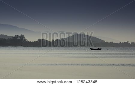 Silhouetted Fishing Boat Showing Misty Mountains Early Morning Sun.