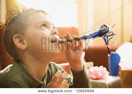 Caucasian junge auf Geburtstagsfeier Noisemaker weht.
