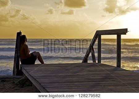 Girl sitting in stairs made of wood at sunset in the beach