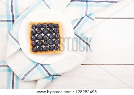 Tartlet with bluebarries and custard on a white plate over a blue checkered napkin and wooden background