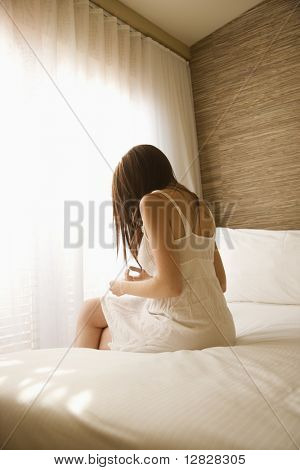 Jolie jeune femme de race blanche, assis sur le lit portant la chemise de nuit.