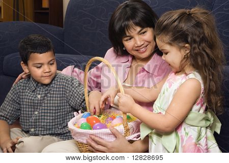Hispanische Mutter mit ihrem jungen und Mädchen zu Hause Blick durch Ostern Korb.