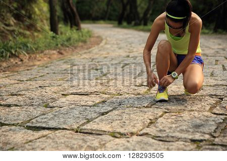 young woman runner tying shoelaces on stone trail