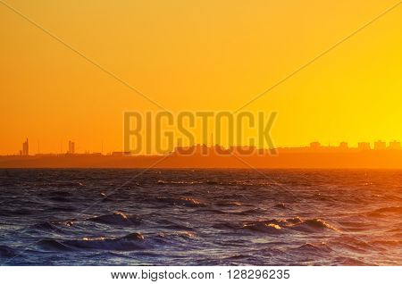 Beautiful red sunset over the sea with urbun city buildings at the horizon