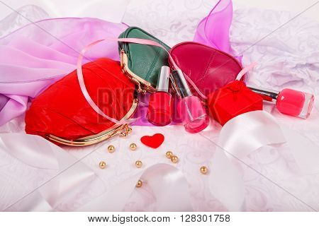 bottles of nail polish on a pink matter with white satin ribbons and female red purse