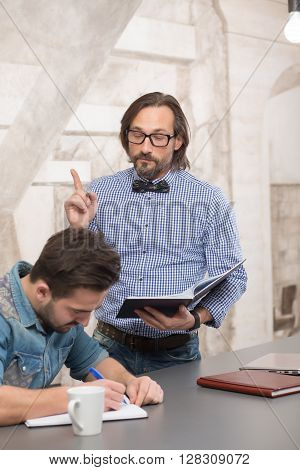 Hnadsome boss in glasses telling his worker nformation for work in office. Demanding man making his worker work.