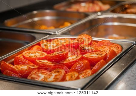 Fresh grilled red tomatoes on a salf service counter in a buffet restaurant in a hotel during breakfast service in the morning